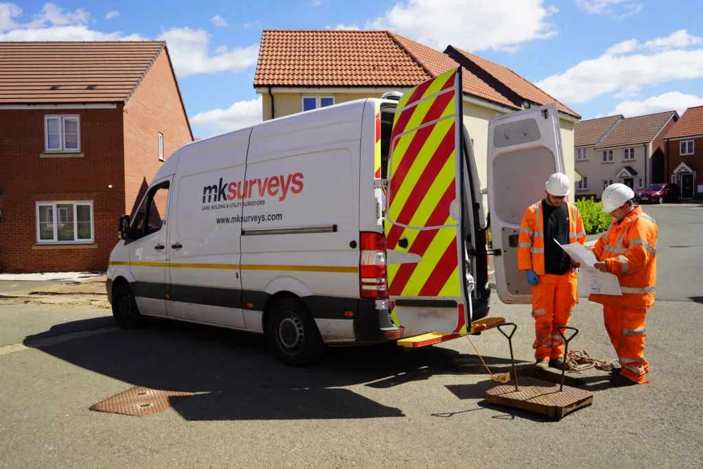 Two men in high vis clothing at the back of a MK Surveys van reviewing plans for a CCTV survey