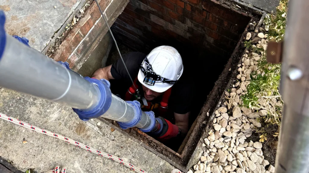 Man climbing a ladder into a manhole for a confined space survey
