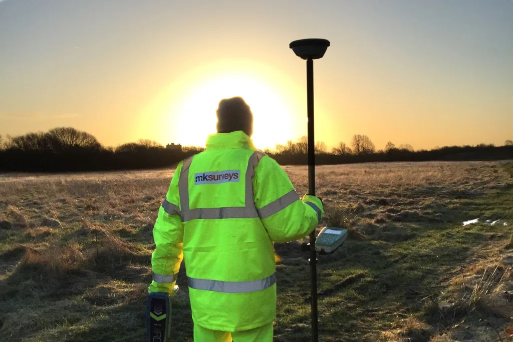 Man performs a Topographical survey in a field with the sunsetting in the distance